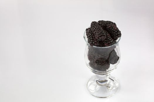 Ripe blackberry are arranged in a clear glass on a light background, a picture in a high key