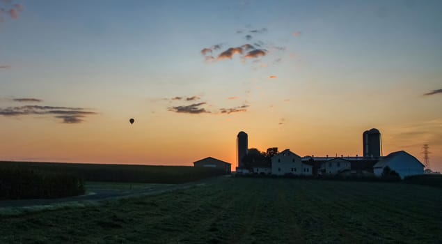 Sunrise Over an Amish Farm with Blues and Reds With a Hot Air Balloon Floating By on a Clear Summer Morning