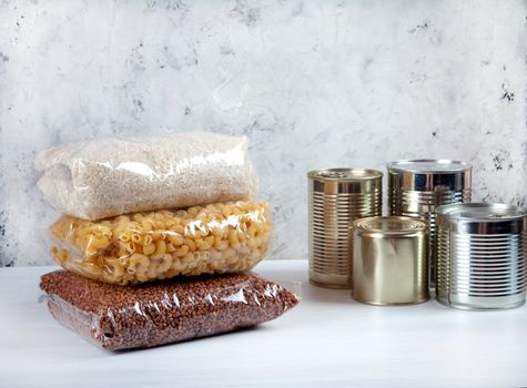 humanitarian assistance for poor and large families. Donation during crisis, pandemic or quarantine. Tin cans, canned food, stew, buckwheat, rice and pasta in transparent bags on white background.