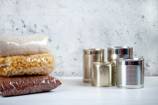 humanitarian assistance for poor and large families. Donation during crisis, pandemic or quarantine. Tin cans, canned food, stew, buckwheat, rice and pasta in transparent bags on white background.