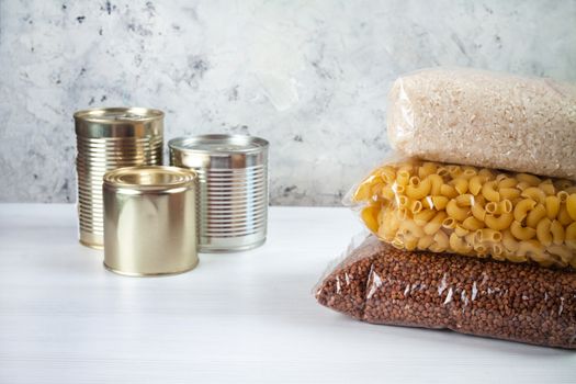 humanitarian assistance for poor and large families. Donation during crisis, pandemic or quarantine. Tin cans, canned food, stew, buckwheat, rice and pasta in transparent bags on white background.