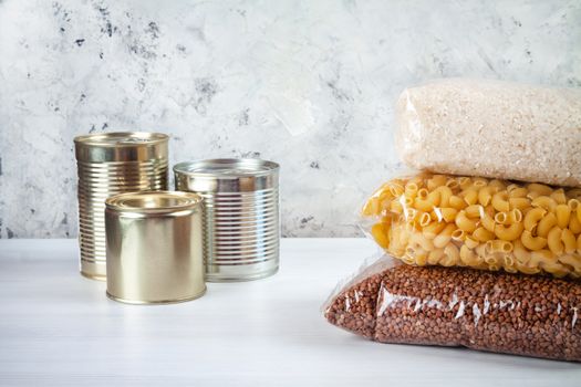 humanitarian assistance for poor and large families. Donation during crisis, pandemic or quarantine. Tin cans, canned food, stew, buckwheat, rice and pasta in transparent bags on white background.