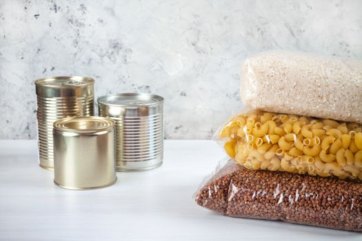 humanitarian assistance for poor and large families. Donation during crisis, pandemic or quarantine. Tin cans, canned food, stew, buckwheat, rice and pasta in transparent bags on white background.