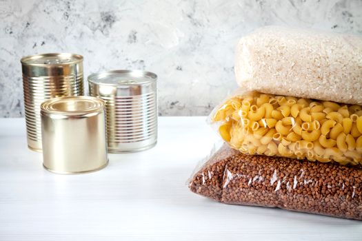 humanitarian assistance for poor and large families. Donation during crisis, pandemic or quarantine. Tin cans, canned food, stew, buckwheat, rice and pasta in transparent bags on white background.