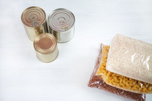 humanitarian assistance for poor and large families. Donation during crisis, pandemic or quarantine. Tin cans, canned food, stew, buckwheat, rice and pasta in transparent bags on white background.