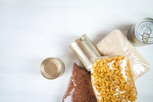humanitarian assistance for poor and large families. Donation during crisis, pandemic or quarantine. Tin cans, canned food, stew, buckwheat, rice and pasta in transparent bags on white background.