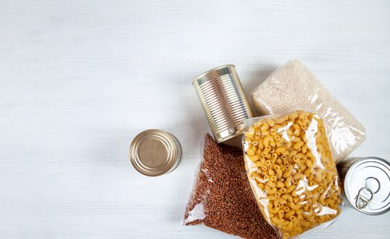humanitarian assistance for poor and large families. Donation during crisis, pandemic or quarantine. Tin cans, canned food, stew, buckwheat, rice and pasta in transparent bags on white background.