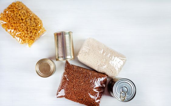 humanitarian assistance for poor and large families. Donation during crisis, pandemic or quarantine. Tin cans, canned food, stew, buckwheat, rice and pasta in transparent bags on white background.