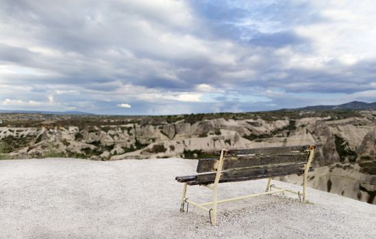 A wooden weathered bench stands against the backdrop of the mountain scenery of Cappadocia