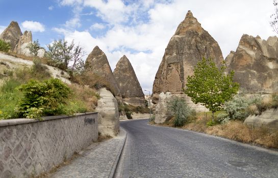 A winding road from paving stones passes near the stone cone houses in the ancient rocks of Goreme, Kappadoki. Rural landscape in the rural way of life of old mountain formations.