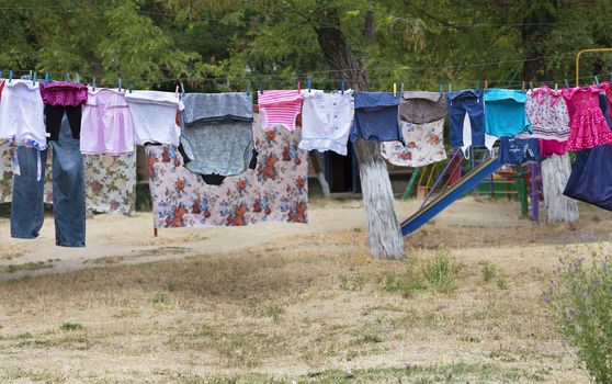 Washing clothes hang on the rope and dry outside over the faded grass in the courtyard of the street