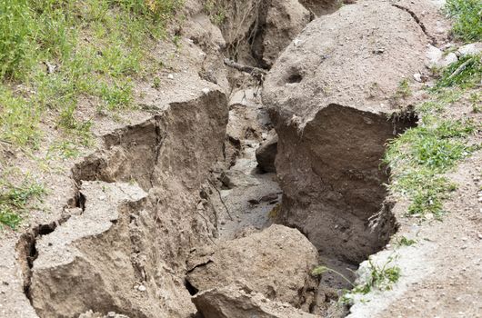 Erosion, destruction of soil on a mountain path after heavy rain among green vegetation.