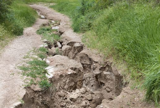 Erosion, destruction of soil on a mountain path after heavy rain among green vegetation.
