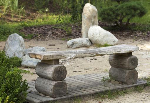 An old wooden bench, green bushes, bonsai trees in a Japanese rock garden