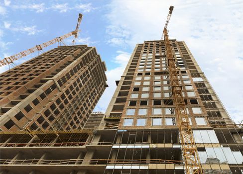 Fragment of facade a house under construction, modern building is under construction, tower building cranes are directed upwards