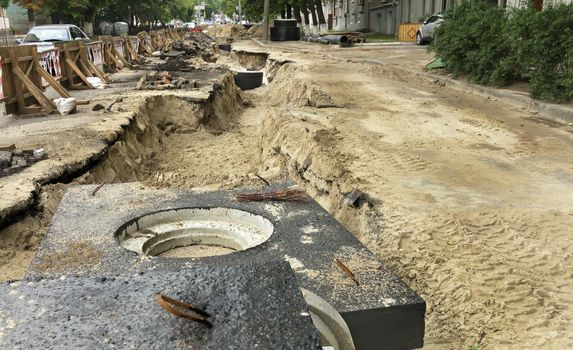 Concrete blocks, wells and pipes of the city collector lie near the excavated trench on the roadway of the street