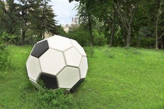 Metal stylized soccer ball on a green lawn in a clearing among the city park