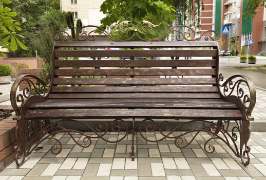 The street wooden bench is painted in bronze color with a metal frame and beautiful forged ornament and elements.