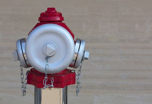 The head of the fire red hydrant with frosted steel caps on the background of the granite wall close-up