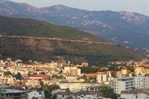 View of the modern city of Budva on the background of a sea bay and a mountain chain in the bright rays of the setting sun