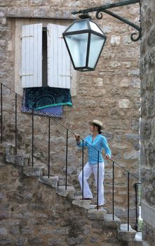 A young woman in a bright turquoise blouse and a straw hat is rising up the stone steps of the old town of Budva, Montenegro