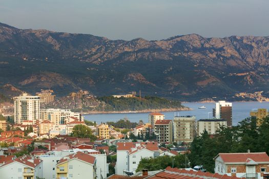 View of the modern city of Budva on the background of a sea bay and a mountain chain in the bright rays of the setting sun