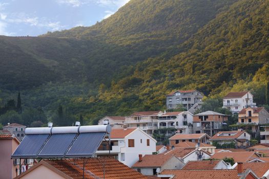 Modern renewable solar water heaters are installed on the orange tile roof of the house against the background of a mountain landscape in Montenegro