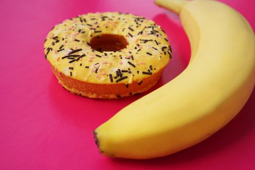 Yellow banana and donut on bright pink background. Above view