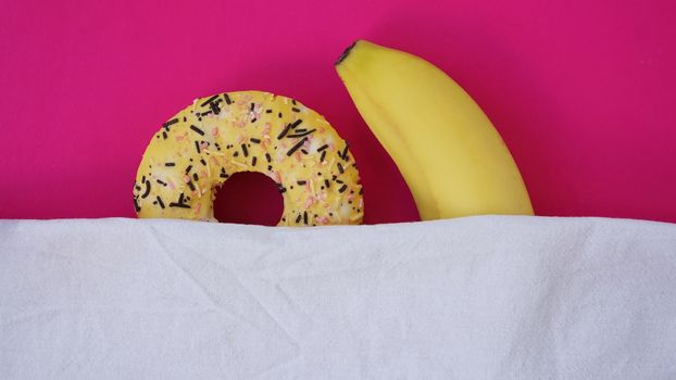 Sweet donut and banana on pink color background. Sex and Erotic concept. Banana hugs donut in bed