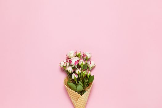 Small roses in waffle cone on pink background, copy space. Minimal style flat lay. For greeting card, invitation. March 8, February 14, birthday, Valentine's, Mother's, Women's day concept. Top view.