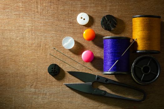 Needle and threads against plastic button and thread cutting scissors on wooden table. Top view and copy space for text. Concept of tailor or Designer.