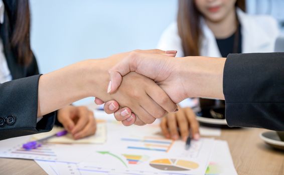 Business people shaking hands on a desk with a computer in the back