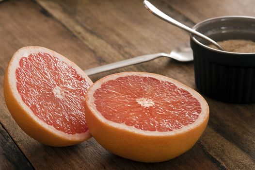 Halved fresh pink grapefruit with a bowl of brown sugar on a wooden table ready to be served for a healthy breakfast rich in vitamin C