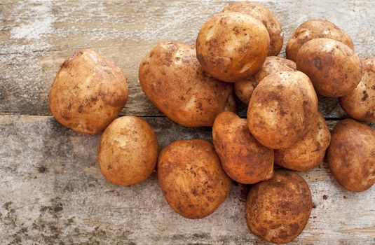 Pile of uncleaned fresh whole farm potatoes on a rustic wooden table at market in a healthy or vegetarian diet concept