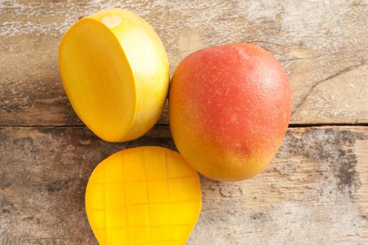 Ripe sliced and whole sweet tropical mango fruit on a rustic wooden table for a healthy seasonal summer diet