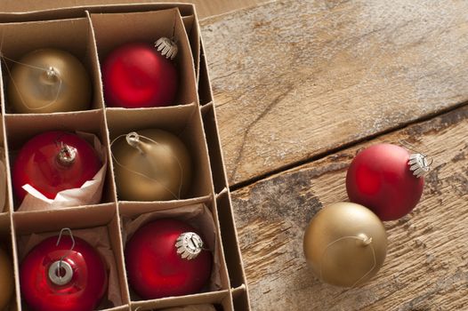 Boxed red and gold Christmas baubles with two decorations outside the box on a rustic wooden table with copy space for your seasonal greeting