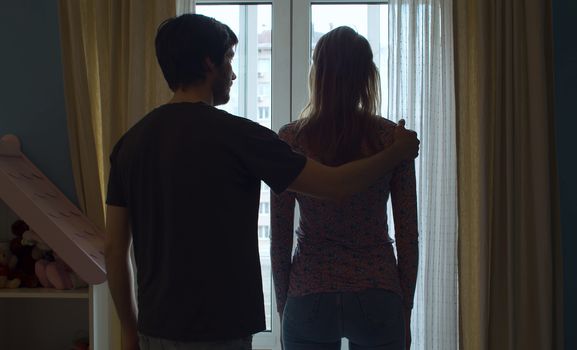 Silhouette of couple near the window. Husband puts hand on wife's shoulder in search of reconciliation.