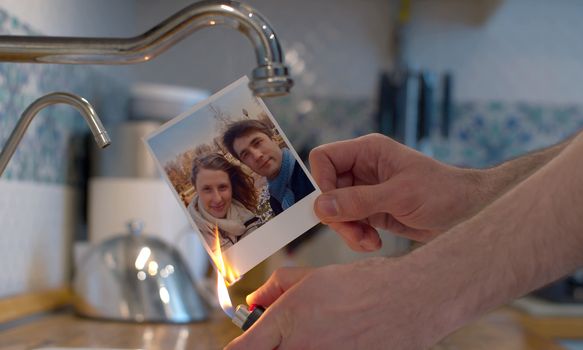 Close up male hands burning a family photo in the kitchen sink. Couple quarreled, divorce