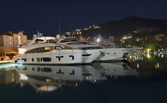 Night on the sea pier with many moored luxury and expensive yachts in the port of Budva, Montenegro.