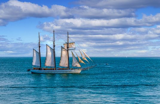 Schooner under sails sailing across a bay under beautiful skies