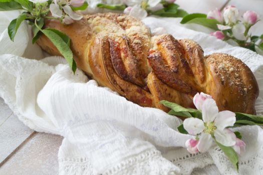 Sweet wicker bun with strowberry on shabby wooden table with lacy knitted napkin and spring flowers.