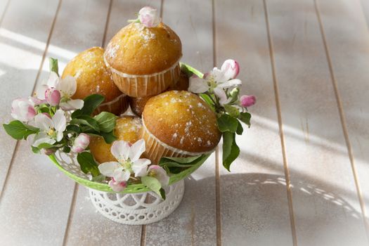 Small freshly muffins in lace wicher basquet and spring flowers on shabby table, copy space