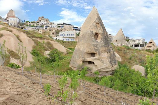 Residential conical caves in the mountains of Cappadocia against the backdrop of modern architecture and blue cloudy sky