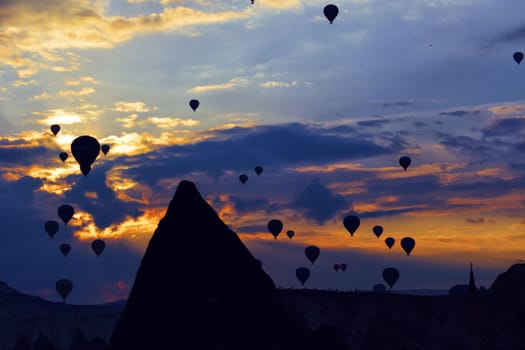 Spectacular view of dozens of flying balloons in the backlight of the early morning against the backdrop of a bright sunrise and blue sky over the conical cliffs of Cappadocia in central Turkey.