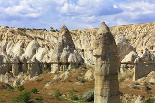 The conical top of the cliff of red and white sandstone powerfully stands out in the landscape of valley in Cappadocia