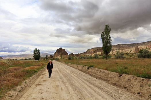 On a dirt sandy road, a tired tourist returns home from a hike through the rocky valleys of Cappadocia.
