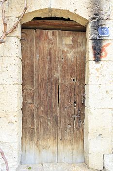 A very old weathered arched wooden door with a metal wrought-iron lock and embedded in an old wall made of shell rock.