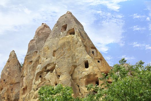Ancient cone-shaped residential caves in a mountain landscape in the valleys of Cappadocia against the bright blue and cloudy spring sky of central Turkey