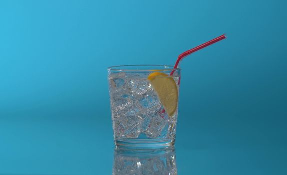 Close up tonic, soda sparkling water in a glass with ice and slice of lemon on a blue background. Refreshing mineral water