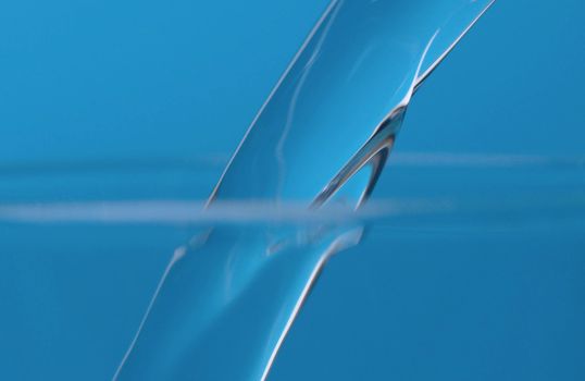 Water jet pouring into a glass. Extreme close up water on blue background.
